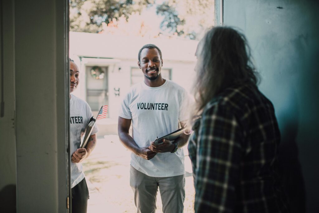 Two diverse volunteers, holding documents, visit a home to offer community support and services.